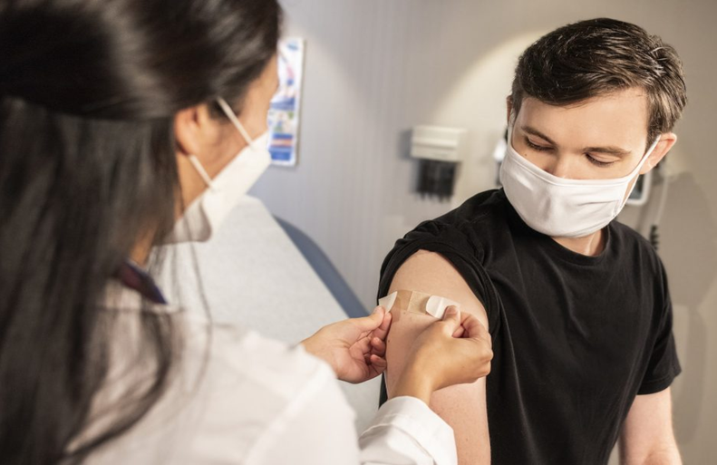 Zdravstvena radnica daje vakcinu mladiću sa maskom.